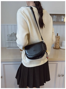 Détail d'un sac besace en cuir noir brillant avec logo et accessoire de charme tressé