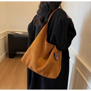 Detail of caramel suede hobo bag with leather strap and heart charm on black coat