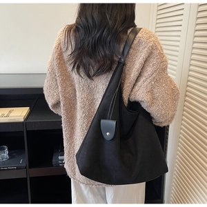 Close-up of black suede tote bag with silver snap button detail on a model