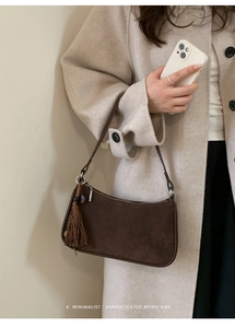 Detail of dark brown suede shoulder bag featuring a stylish tassel and silver metal zipper
