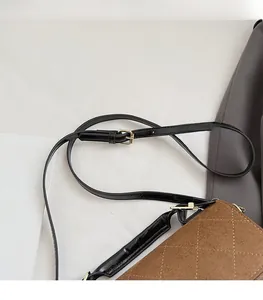 Détail de la bandoulière en cuir noir et de la boucle en métal doré sur le sac brun