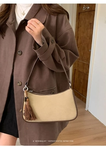 Detail of retro beige baguette bag with brown leather trim and fringe tassel charm