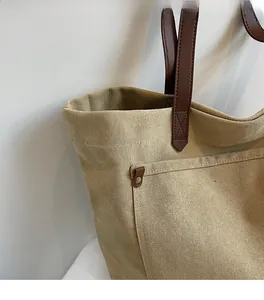 Detail of khaki canvas tote bag featuring brown faux leather straps and metal rivets