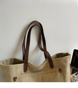 Detail of canvas tote bag with brown leather strap and front pocket with metal button