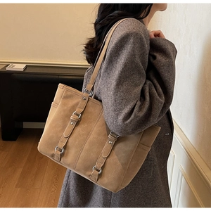Detail view of khaki suede tote bag featuring decorative straps and metal rings