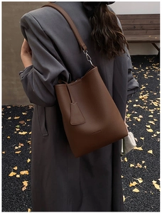 Mannequin portant un sac seau en cuir marron foncé dans une rue avec des feuilles de ginkgo