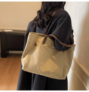 Detail of canvas tote bag with brown leather handles and front pocket in a room