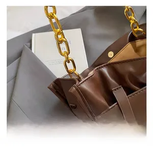 Detail of a brown leather pleated handbag featuring a thick gold metal chain strap