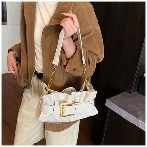 Detail of cream pleated shoulder bag featuring a bold gold buckle and chunky chain strap