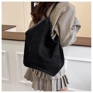 Detail of a large black suede tote bag styled with a grey blazer for a minimalist look