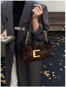 Close-up of a dark brown ruched handbag featuring a gold buckle and chain shoulder strap