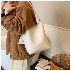 Détail du sac seau crème avec texture litchi et logo de marque porté par un mannequin