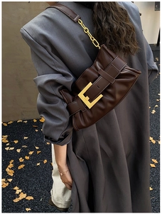Detail of a dark brown pleated shoulder bag with a large gold buckle and metal chain strap