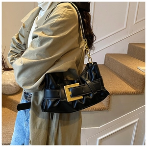 Detail of black pleated shoulder bag with oversized gold buckle on a trench coat
