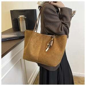 Close-up of brown suede tote bag featuring unique beaded tassel and vertical stitching details
