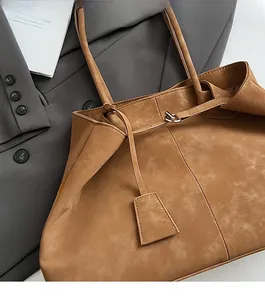 Detail of a brown suede tote bag with metal clasp and tag on a grey blazer background
