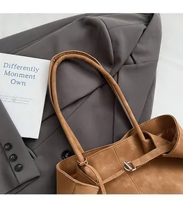 Close-up of brown frosted tote bag with metal buckle on grey blazer and magazine