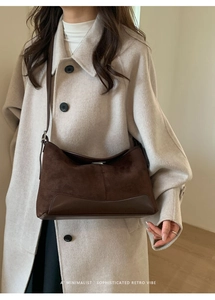 Detail of dark brown suede and leather crossbody bag styled with a minimalist beige coat