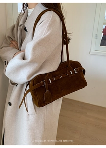 Close-up of retro brown suede underarm bag with silver buckles worn with a beige coat