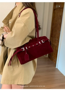 Close-up of burgundy suede shoulder bag with silver buckles on a trench coat