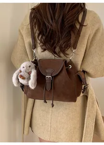 Brown faux suede crossbody bucket bag with drawstring and plush bunny charm on a model