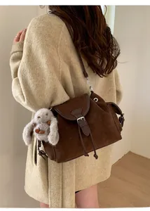 Detail of brown matte bucket bag with vintage metal buckle and plush rabbit charm