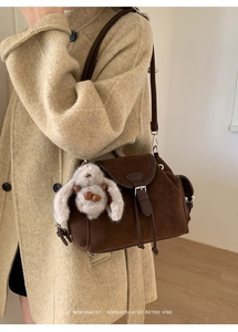 Detail of dark brown suede crossbody bag with plush rabbit pendant and leather trim
