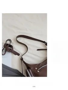 Detail view of adjustable wide shoulder strap on brown leather crossbody bag with silver zipper