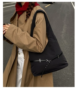 Detail of black nylon tote bag with leather strap and metal hook on model in autumn trench