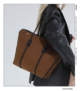 Detail of a large brown suede tote bag with intricate black braided shoulder straps