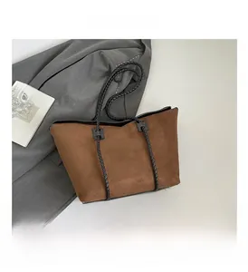 Detail of a brown suede tote bag with black woven handles and metal base studs
