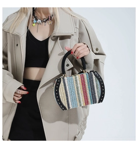 Detail shot of colorful woven straw bag with gold studs and hard black handle