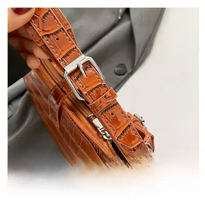 Detail of adjustable strap with silver buckle on brown crocodile texture shoulder bag
