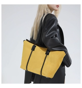 Close-up of yellow suede tote bag with black woven handles on a model in leather jacket