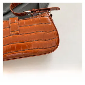 Close-up of brown croc-embossed leather texture and fine stitching on a punk crossbody bag