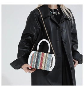 Detail of colorful woven handbag featuring a white handle and gold chain strap