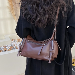 Detail of a dark brown leather crossbody bag with silver zippers on a black coat