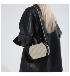 Detail of woven straw handbag featuring black leather trim with gold studs and chain strap