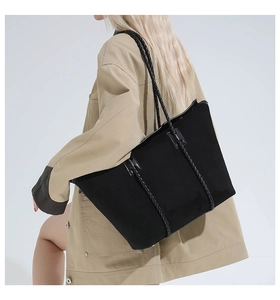 Detail of a large black matte tote bag with woven handles on a khaki trench coat