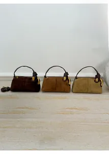 Detail view of suede pillow bags in dark brown, caramel, and olive green with gold buckles