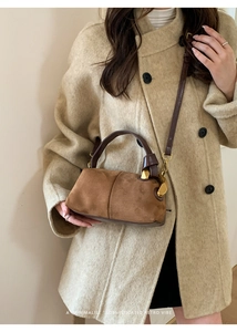 Detailed view of a brown suede bowling bag with leather handles and gold metal hardware