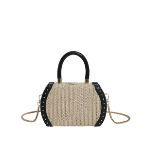 Detail of straw box bag with black leather edges, gold rivets and chain strap
