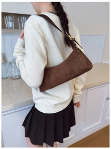 Close-up of brown suede underarm bag with adjustable strap worn by model in home setting