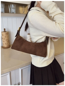 Detail of brown suede shoulder bag with contrast stitching and golden metal buckle strap