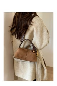 Close-up of brown suede Boston bag with gold ring detail on beige wool coat