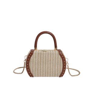 Detail of straw woven handbag featuring brown leather trim and golden rivets