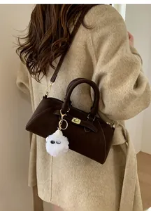 Dettaglio borsa a conchiglia in pelle marrone scuro con chiusura dorata e ciondolo peluche
