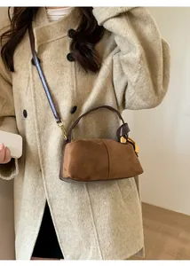 Brown suede pillow bag with golden hardware worn over a beige coat by a model