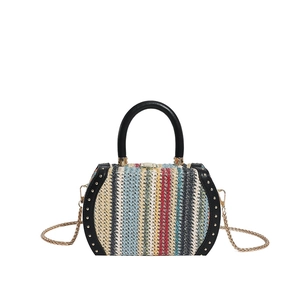 Detail of colorful woven straw bag featuring black leather handles and rivet trim accents