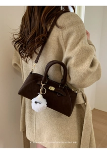 Borsa a conchiglia marrone opaco con chiusura dorata e ciondolo di peluche su modella